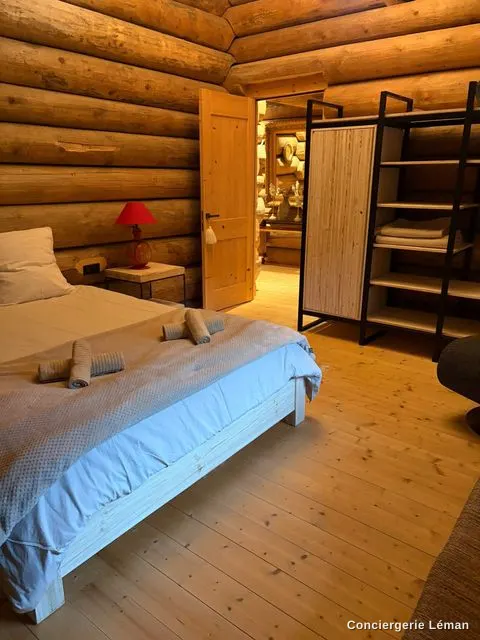 Chambre de chalet en rondins : lit fait, serviettes posées sur le plaid