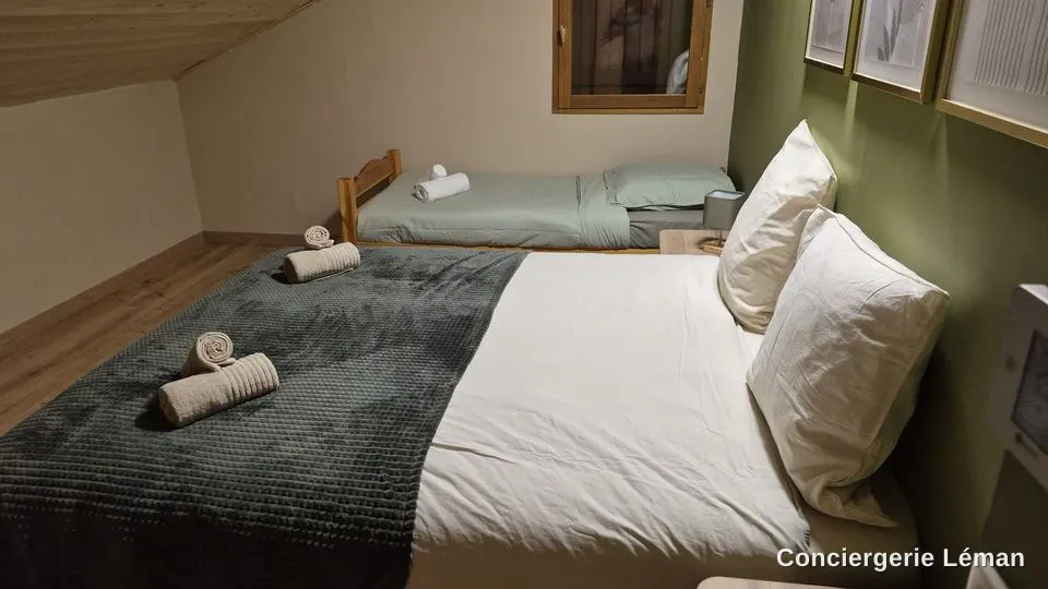 Chambre sous les combles : lit double et lit simple faits, serviettes roulées
